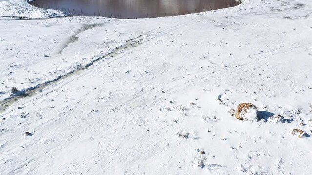 Mt Hermon, Israel. Fly in drone shot over a snowy valley to a crater lake, Birkat Ram. Hikers can be seen around the lake. Background is snow covered mountains and blue sky.