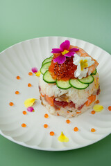 Chirashizushi sushi cake with salmon roe and edible flowers on a light green background