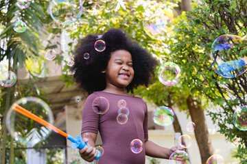 African American girl playing, blowing super big soap bubbles, having fun on backyard.