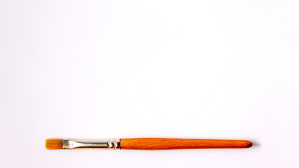 Flat lay of artistic orange metal wooden paint brush close up on white background with copy space from above. Drawing and design concept work tools
