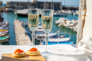 Pairing of blinis with sour cream and salted salmon red caviar and French champagne brut sparkling wine and served with view on colorful boats in harbor of Cassis, Provence, France - obrazy, fototapety, plakaty