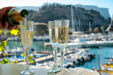 Pouring in three glasses of French champagne sparkling wine and view on colorful fisherman's boats...