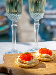 Pairing of blinis with sour cream and salted salmon red caviar and French champagne brut sparkling wine and served with view on colorful boats in harbor of Cassis, Provence, France