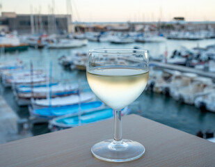 Cold white wine from Cassis region served in glass on outdoor terrace with view on old fisherman's harbour with colourful boats in Cassis, Provence, France
