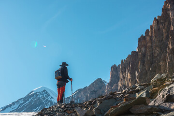 Scenic alpine landscape with silhouette of hiker with trekking poles against large sharp rocks and...