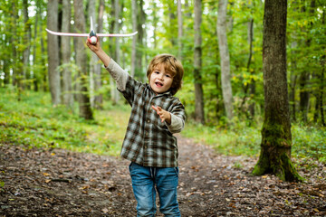 Child 6 year old pilot with toy airplane dreams of traveling in summer in nature. Kids dreams. Child plays with a toy plane and dreams of becoming a pilot.