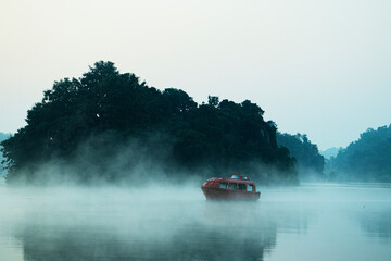 A passenger boat floating in a foggy lake in morning 