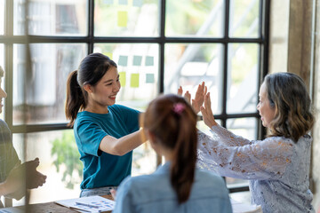 Diverse group of smiling young business people celebrating success with high fives while working together in a modern office, colleagues celebrate shared business success or victory in office.
