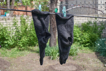 Leaky socks hang on a rope in the yard of a village house. Black socks with holes in the heel hang...