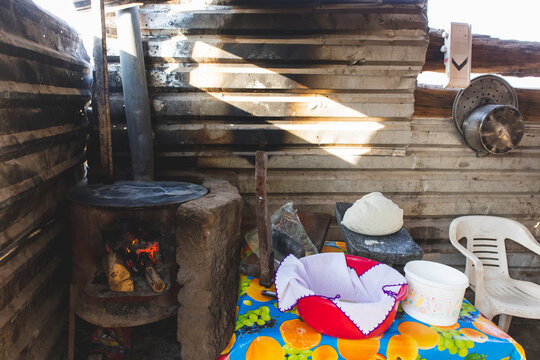 Mujer mexicana torteando maza de maíz en un metate y una estufa de leña para hacer tortillas caseras  