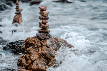 Concept of balance and harmony. Cairn stack of stones pebbles cairn on coast amid the crashing waves. Meditative art of stone stacking