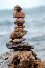 Concept of balance and harmony. Cairn stack of stones pebbles cairn on coast amid the crashing waves. Meditative art of stone stacking