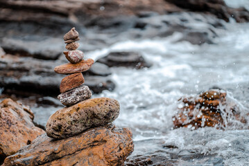 Concept of balance and harmony. Cairn stack of stones pebbles cairn on coast amid the crashing waves. Meditative art of stone stacking
