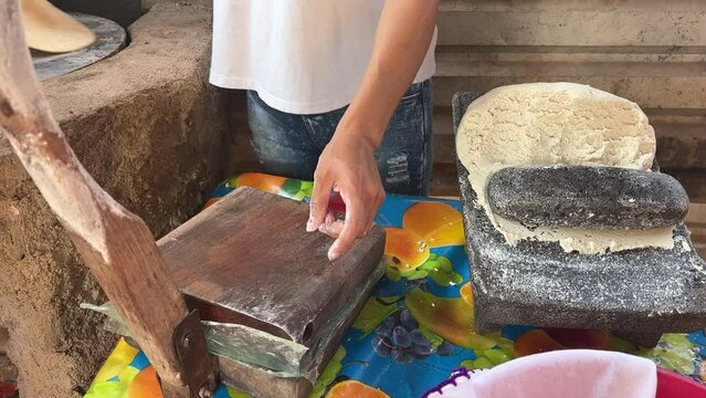 Mujer mexicana torteando maza de ma&iacute;z en un metate y una estufa de le&ntilde;a para hacer tortillas caseras  