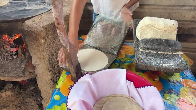 Mujer mexicana torteando maza de ma&iacute;z en un metate y una estufa de le&ntilde;a para hacer tortillas caseras  