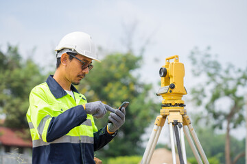 Asian engineers use yellow theodolite to find blueprints at building construction sites.