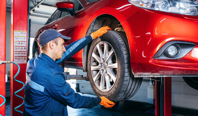 Expert specialist technician changes tires, tyres of lifted up car at auto service, wears uniform costume.
