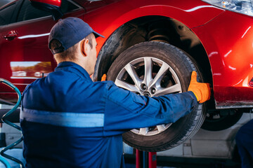 Expert specialist technician changes tires, tyres of lifted up car at auto service, wears uniform...