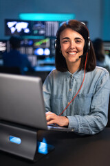 Female caucasian financial analyst working in the office with laptop and headset looking at camera. Vertical.