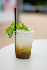 A Plastic glass of Mojito cocktail with lime and mint on white table.