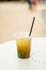 A Plastic glass of Mojito cocktail with lime and mint on white table.