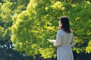 夏の公園で散歩して読書している中年女性の姿