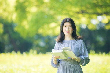 夏の公園で読書している中年女性の姿