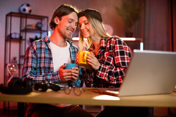 Loving couple touching foreheads at romantic moment sitting at table and watching favorite movie using laptop. Caucasian man and woman enjoy evening leisure at home.