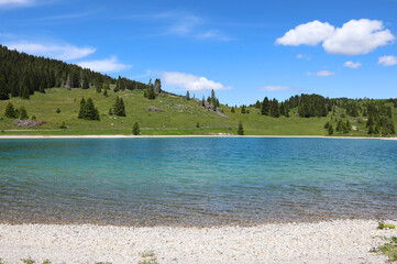 Beautiful lake with clear clear water and alpine mountains in the background - obrazy, fototapety, plakaty