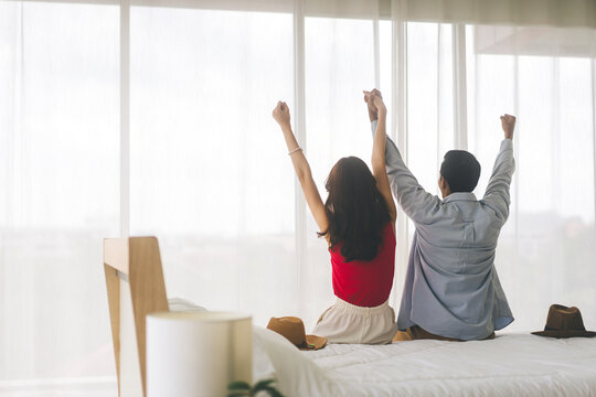 Rear View Of Adult Asian Couple Relax Stretching Arm At Hotel On The Bed.