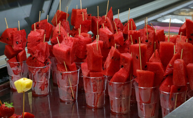 many skewers of large slices of ripe red WATERMELON in the glasses for sale in the alfresco bar of...