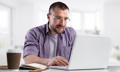 Young smiling man in glasses using laptop sitting at home desk, watching webinar studying online,