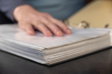 An unfocused shot of a man's hand resting on top of a file folder. Adult Male placed his hand on an open gray folder with a binder. Defocus, noise, grain effect. Selective Focus.