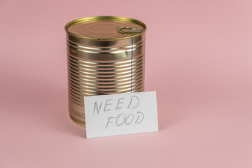Need food. Business card with handwritten text and canned food against a pink background. Gold-colored tin. Concept of helping the needy and hungry. Selective focus.