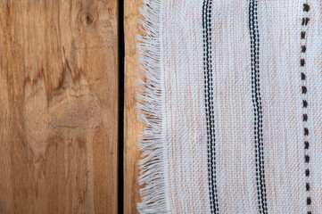 A white kitchen towel lies on the countertop of a wooden table. The fringed towel is fringed and patterned on the rough boards. Top view. Copy space