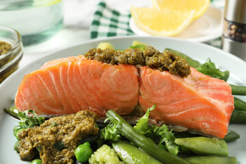 Tasty cooked salmon with pesto sauce and fresh salad on plate, closeup