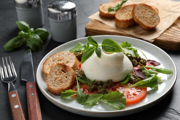 Delicious burrata salad with tomatoes, arugula and pesto sauce served on dark grey table