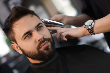 Professional hairdresser working with client in barbershop