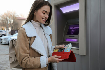 Woman putting money into wallet near cash machine outdoors