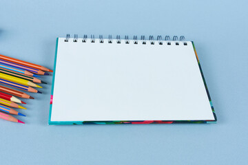 Opened notebook on blue background with colored pencils. 