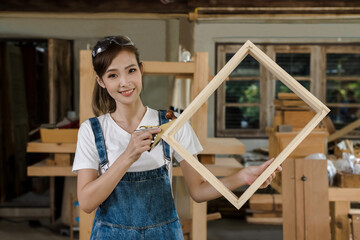 young Asian carpenter woman making DIY wood frame in carpentry workshop