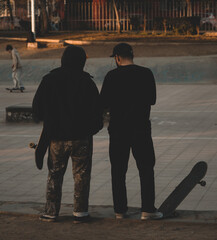 two skater friends chatting as they watch and wait for their turn to do tricks on the skateboard