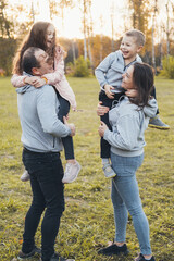 Fototapeta premium Family spending the afternoon together, parents carrying children in their arms as they walk through the park. Happy family leisure. Enjoying weekend. Family