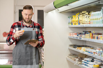 Male supermarket staff checking products using a tablet. Young joyful man food store assistant at...