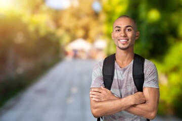 Smiling young student man looking at camera outdoors with backpack standing at university campus