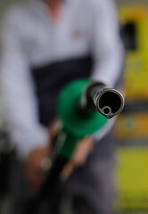 Shallow depth of field (selective focus) details with a man holding a fuel pump dripping with gasoline in a gas station.