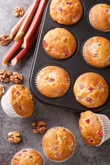 Freshly baked muffins with rhubarb and walnuts close-up in a baking dish on the table. Vertical top view from above