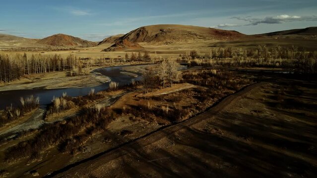 Camera span at low altitude. Landscape from the western. Bare trees without leaves. The river is located in the mountain steppe.