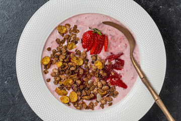White plate with red strawberries, granola and natural yogurt on a black background, top view