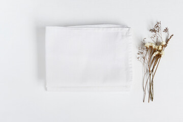 Stack of fabrics with dry flowers over light background. Flat lay with white folded linen cloth for mock up.
